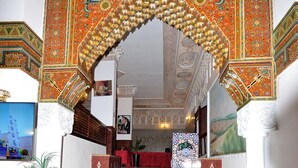 A grand entrance with a red carpet leading to a reception area, featuring intricate tile work and a large archway. - Hôtel Nouzha La perle du tourisme (Fes)