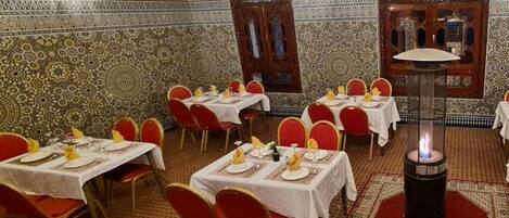 Comedor con mesas dispuestas para cuatro, sillas rojas y paredes decoradas con un patrón ornamentado.