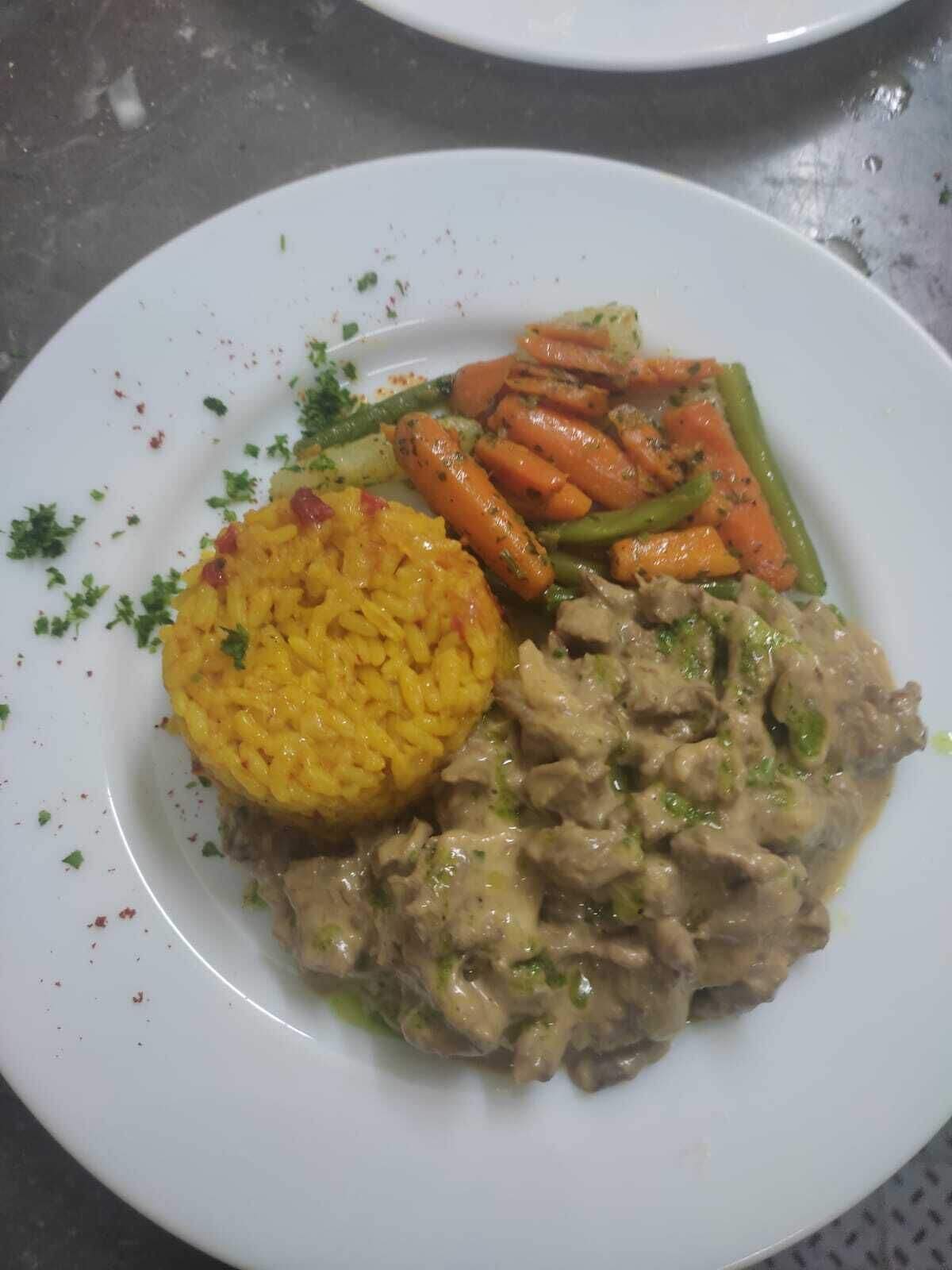 Un plato con arroz amarillo, un guiso de carne y verduras.