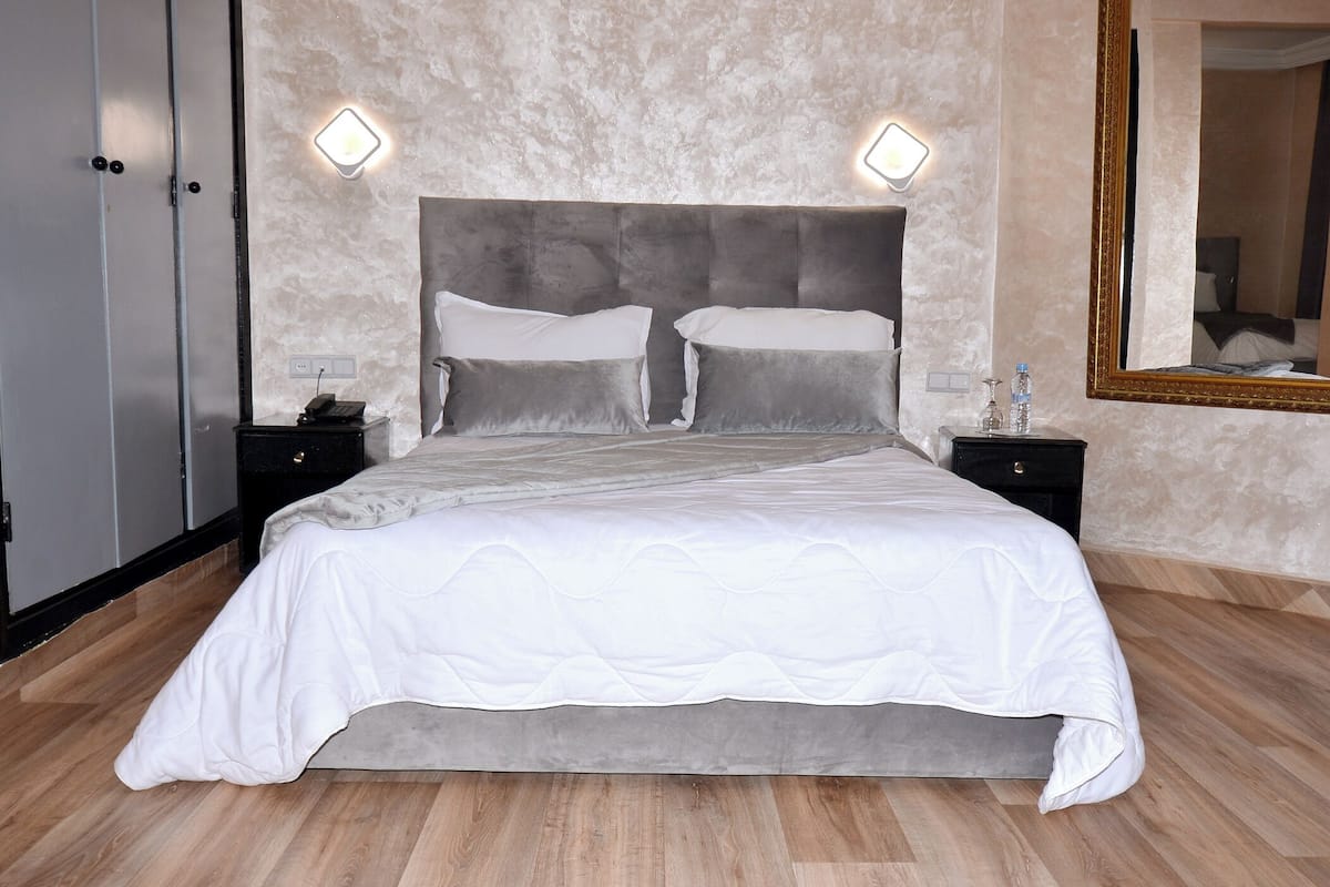 A bedroom with a large bed, two bedside tables, a nightstand, a mirror, and a wardrobe.