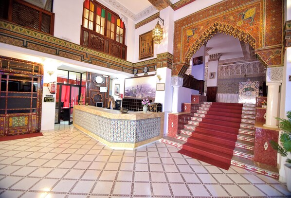 A lobby with a reception desk, a staircase with red carpet, and ornate wall decorations. - Hôtel Nouzha La perle du tourisme (Fes)