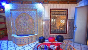 A room with intricate tile patterns, a traditional Moroccan-style door, and a table set with decorative items. - Hôtel Nouzha La perle du tourisme (Fes)