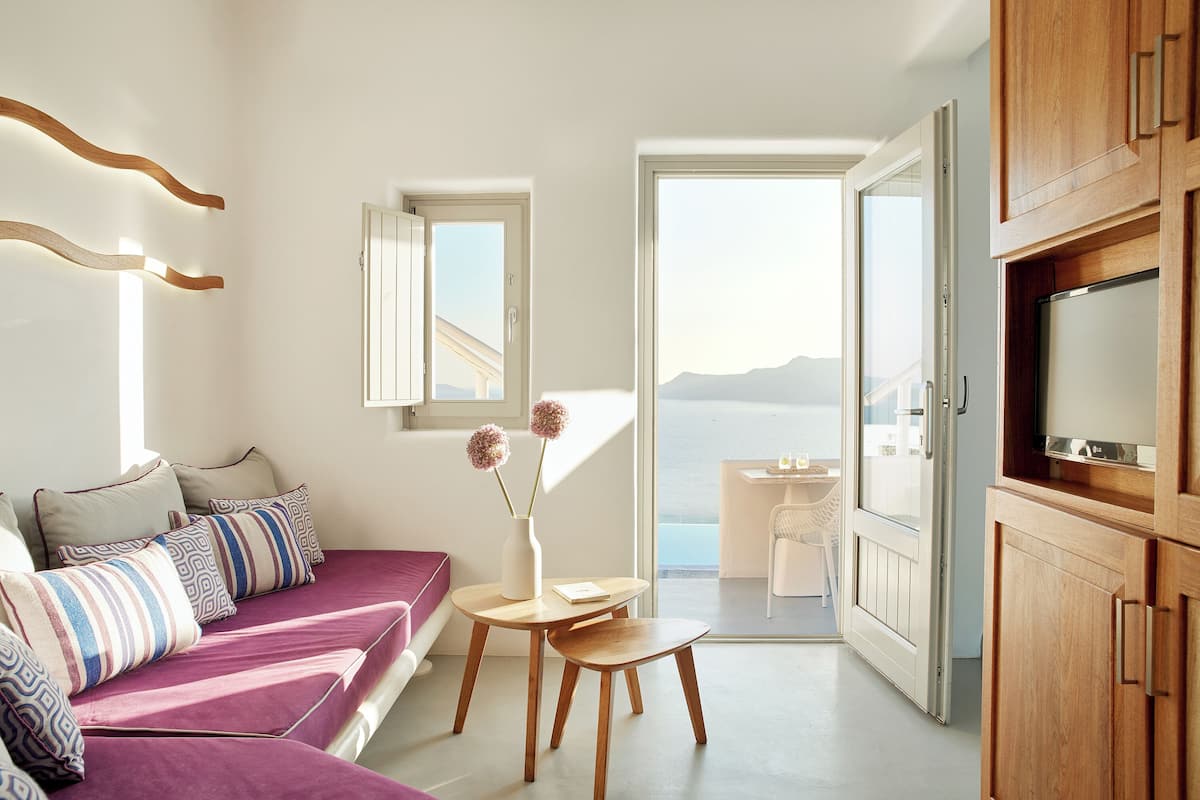 Een moderne woonkamer met een bank, een klein tafeltje met een vaas, en uitzicht op zee door een open deur.