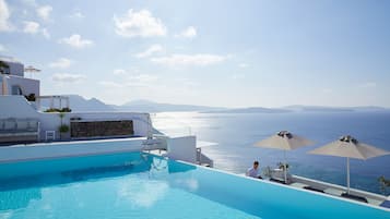 Relax by the infinity pool overlooking the ocean, surrounded by comfortable seating and umbrellas.