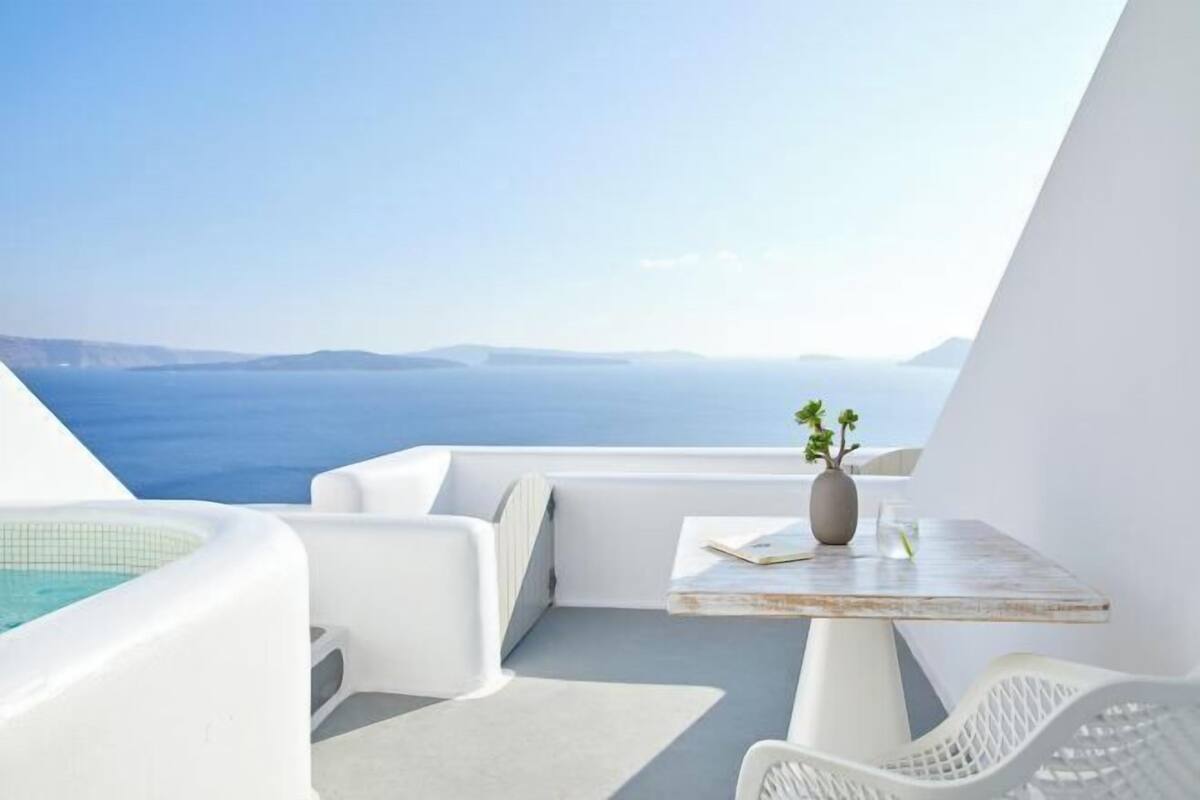Een balkon met witte meubels, een kleine tafel met een vaas en uitzicht op zee.