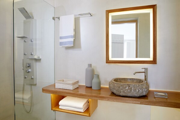 A modern bathroom with a glass-enclosed shower, a wooden vanity with a stone sink, and a mirror with a wooden frame.