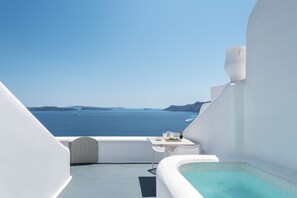 A balcony with a view of the sea, a small table with a chair, and a hot tub. - La Perla Villas and Suites - Adults Only (Santorini)