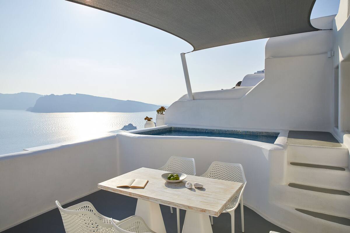 Een balkon met een tafel, stoelen en uitzicht op zee.