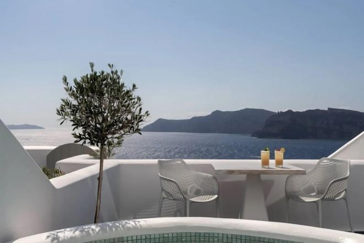 Un balcon avec vue sur la mer, une petite table avec des boissons et une chaise.