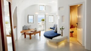 A spacious living area with a sofa, coffee table, and a view of the outdoors. - La Perla Villas and Suites - Adults Only (Santorini)