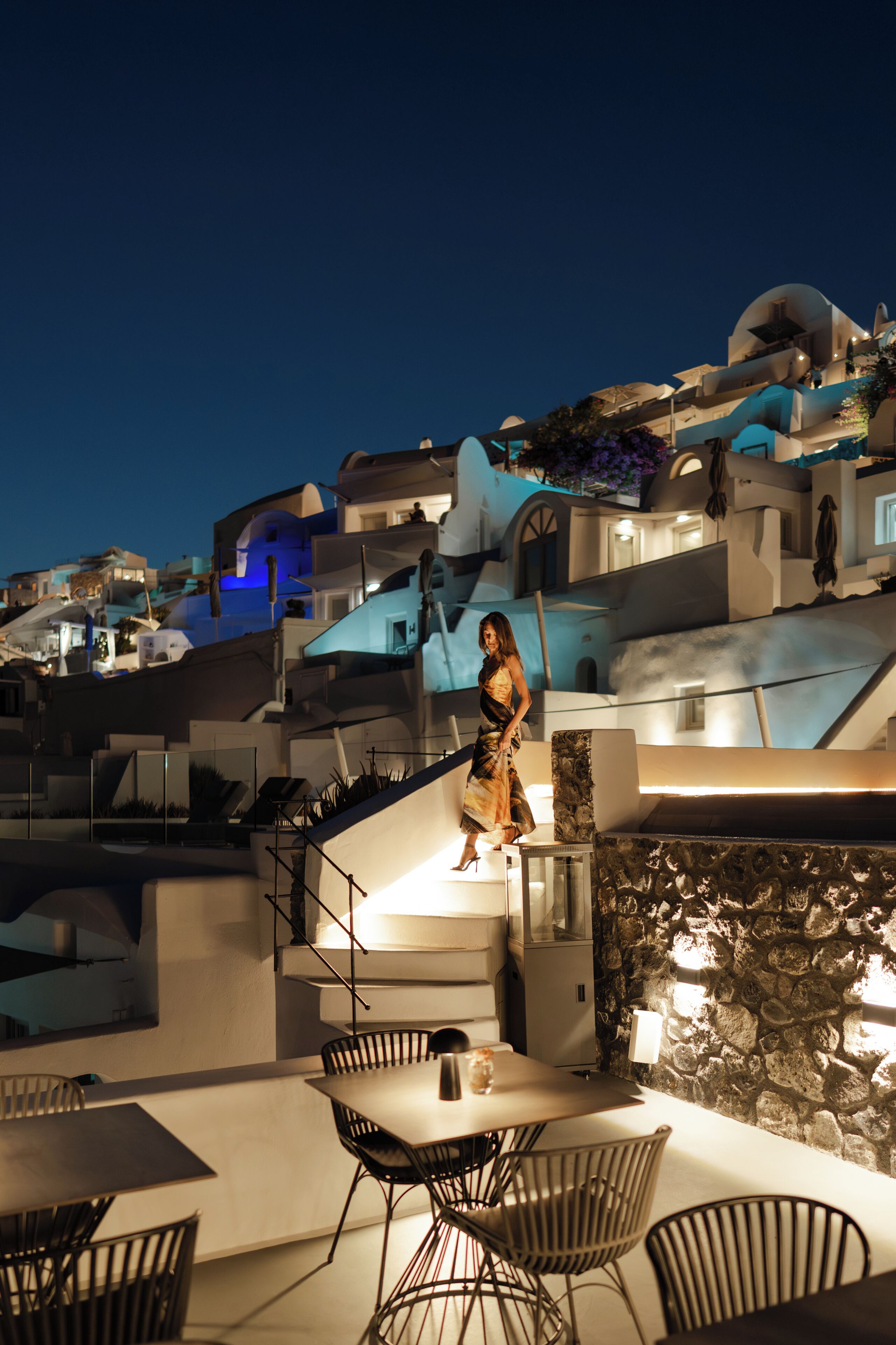 A woman walking on a rooftop terrace with modern architecture and outdoor seating.