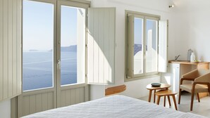 A bedroom with a bed, a desk, a chair, and a view of the sea. - La Perla Villas and Suites - Adults Only (Santorini)