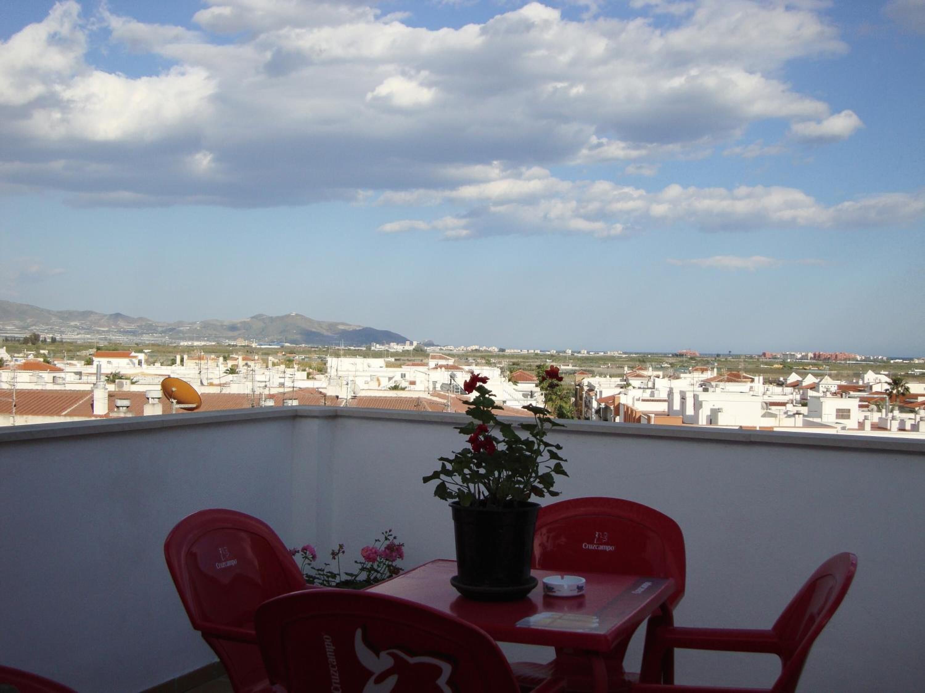 A balcony with red chairs, a table, and a potted plant.