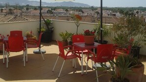 A terrace with red chairs and white umbrellas, potted plants, and a view of the cityscape. - Hostal Palomares (Salobreña)