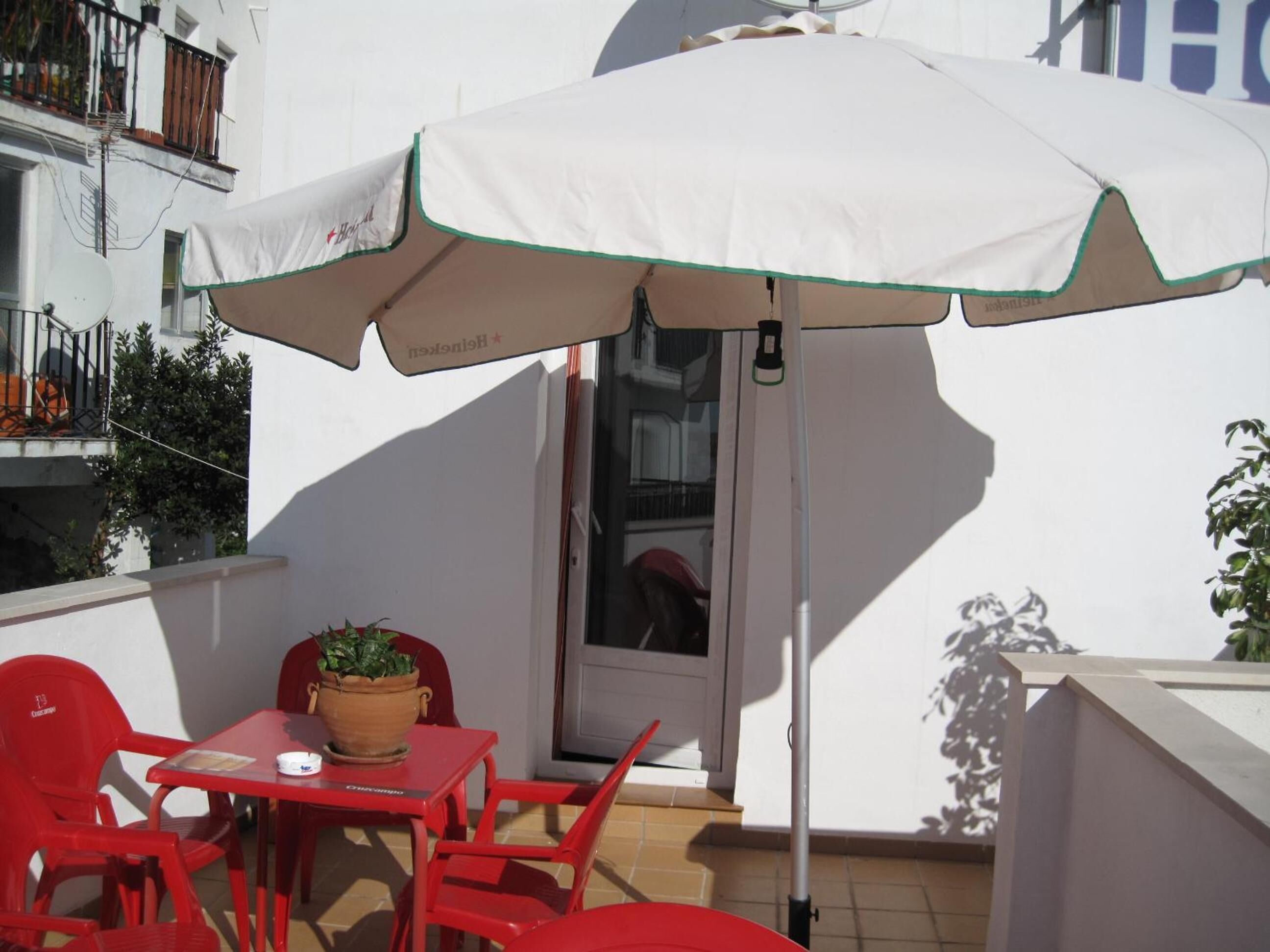 Un pequeño espacio al aire libre con sombrilla blanca, sillas rojas y una mesa con una planta en maceta.