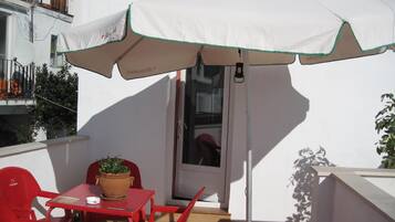Un pequeño espacio al aire libre con sombrilla blanca, sillas rojas y una mesa con una planta en maceta.