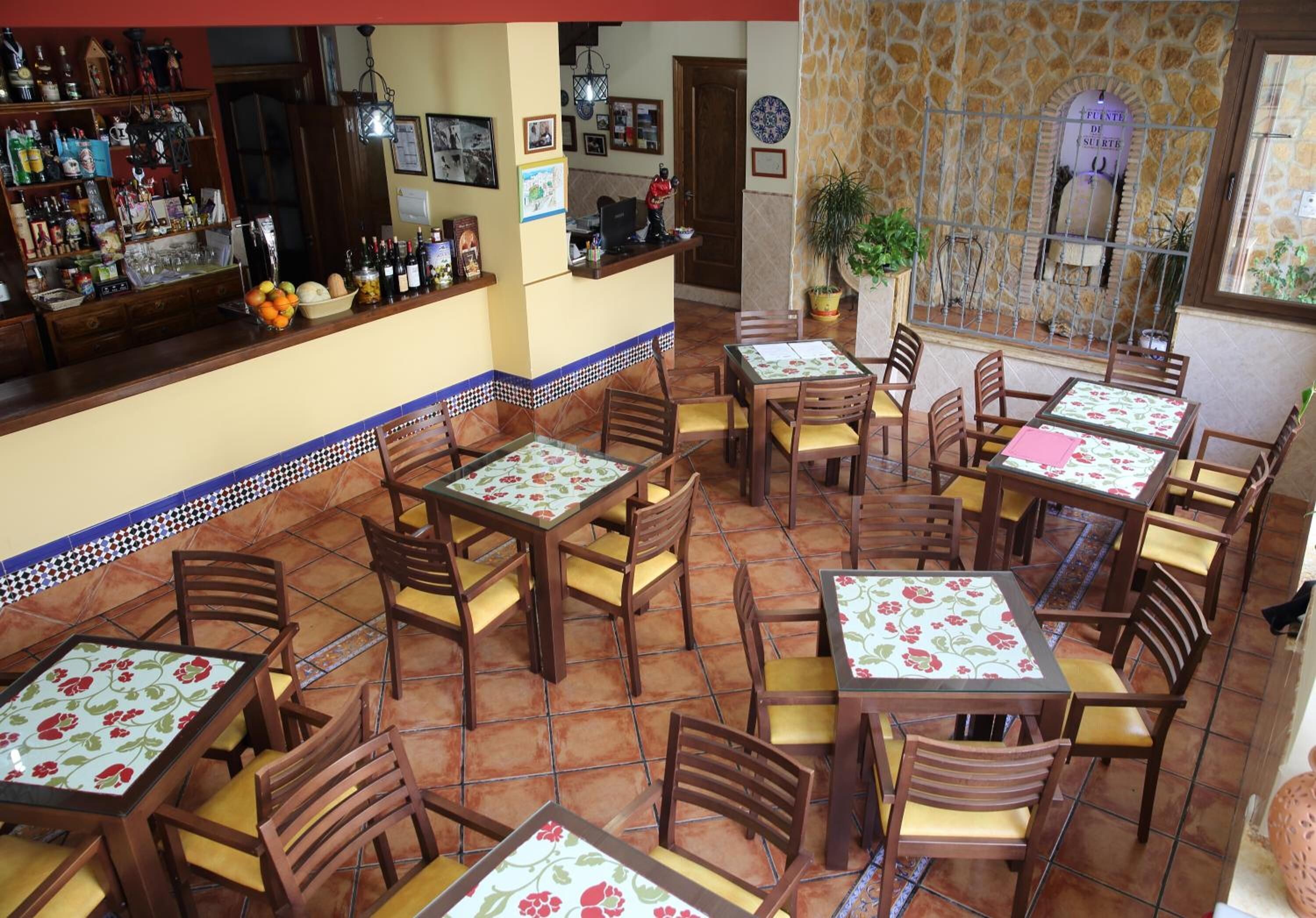 Ein Restaurant mit mehreren Tischen und Stühlen, einer Bar mit verschiedenen Flaschen und einer Steinwand mit einer Pflanze.