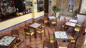 Ein Restaurant mit mehreren Tischen und Stühlen, einer Bar mit verschiedenen Flaschen und einer Steinwand mit einer Pflanze.