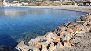 A coastal scene with clear blue water, rocky shoreline, and buildings in the background. - Hostal Palomares (Salobreña)