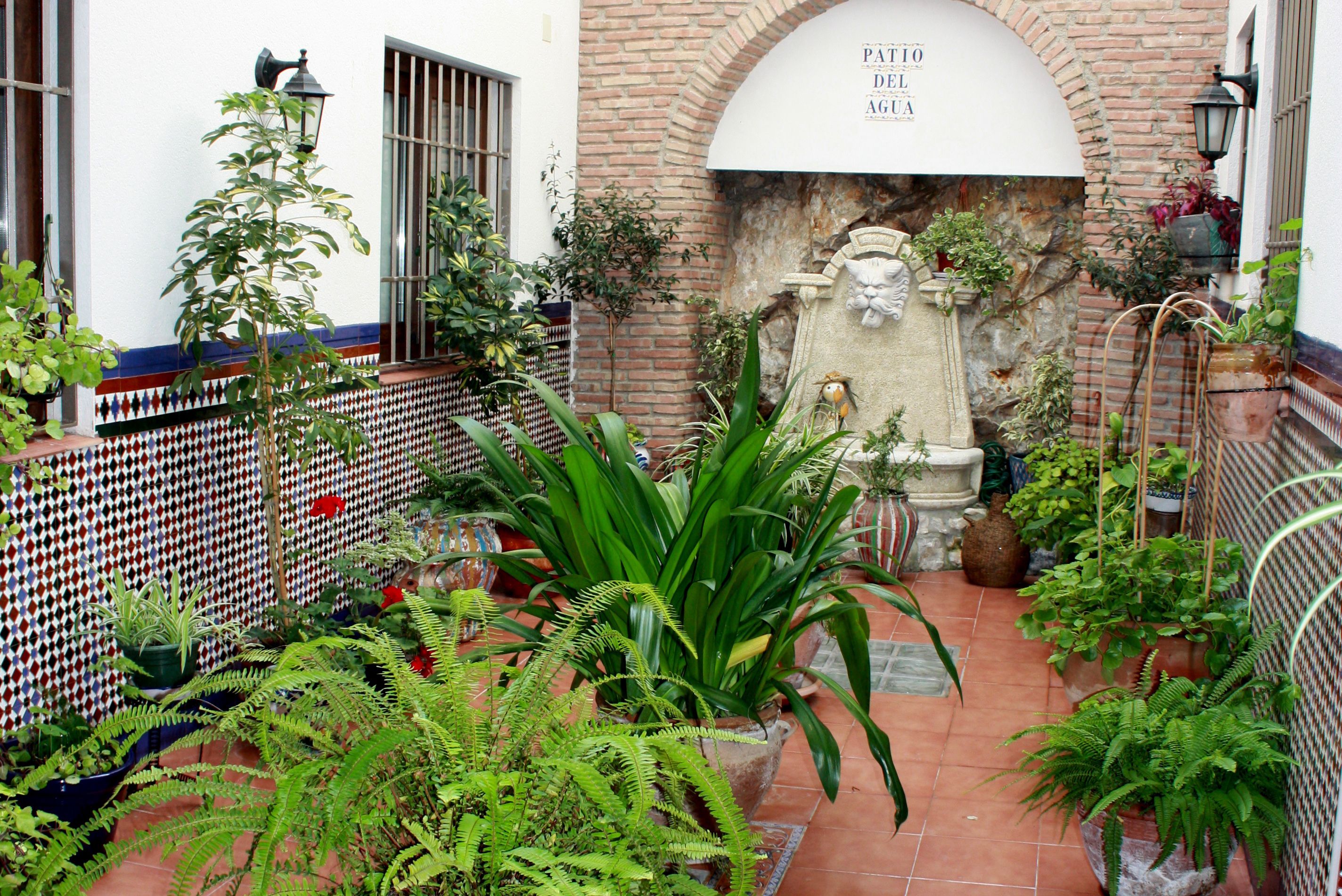 Un patio con plantas en macetas, una fuente de piedra y un muro con azulejos de diseño.