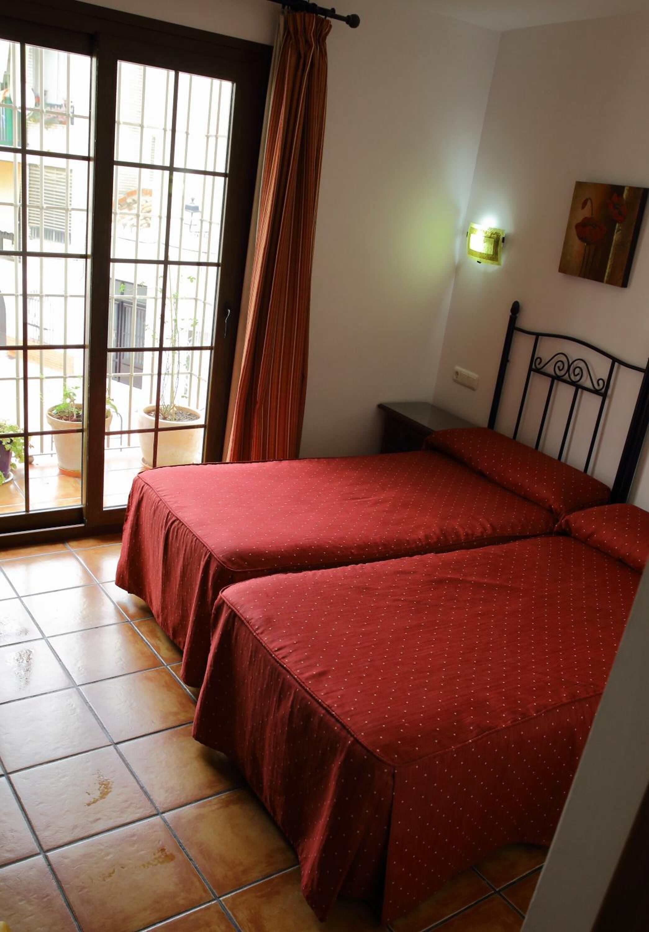 A room with two beds, a sliding glass door to a balcony, a nightstand, and a wall-mounted light.