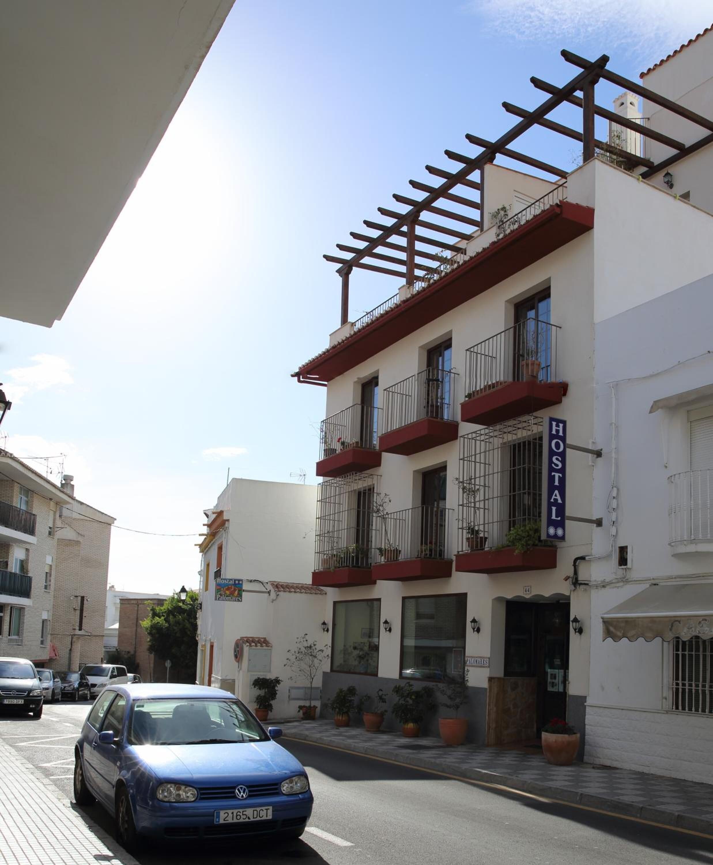 Un edificio con un letrero que dice "HOSTAL" y balcones con macetas de plantas.