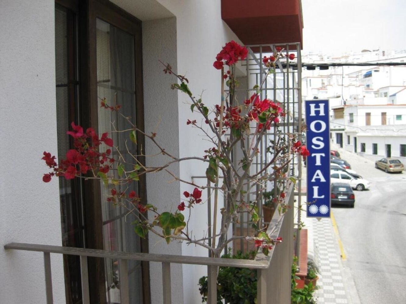 En balkong med röda blommor och en skylt med texten ”HOOSTAL”.