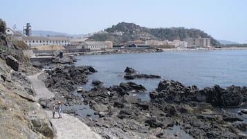 Un camino costero que lleva a una costa rocosa, con edificios al fondo.