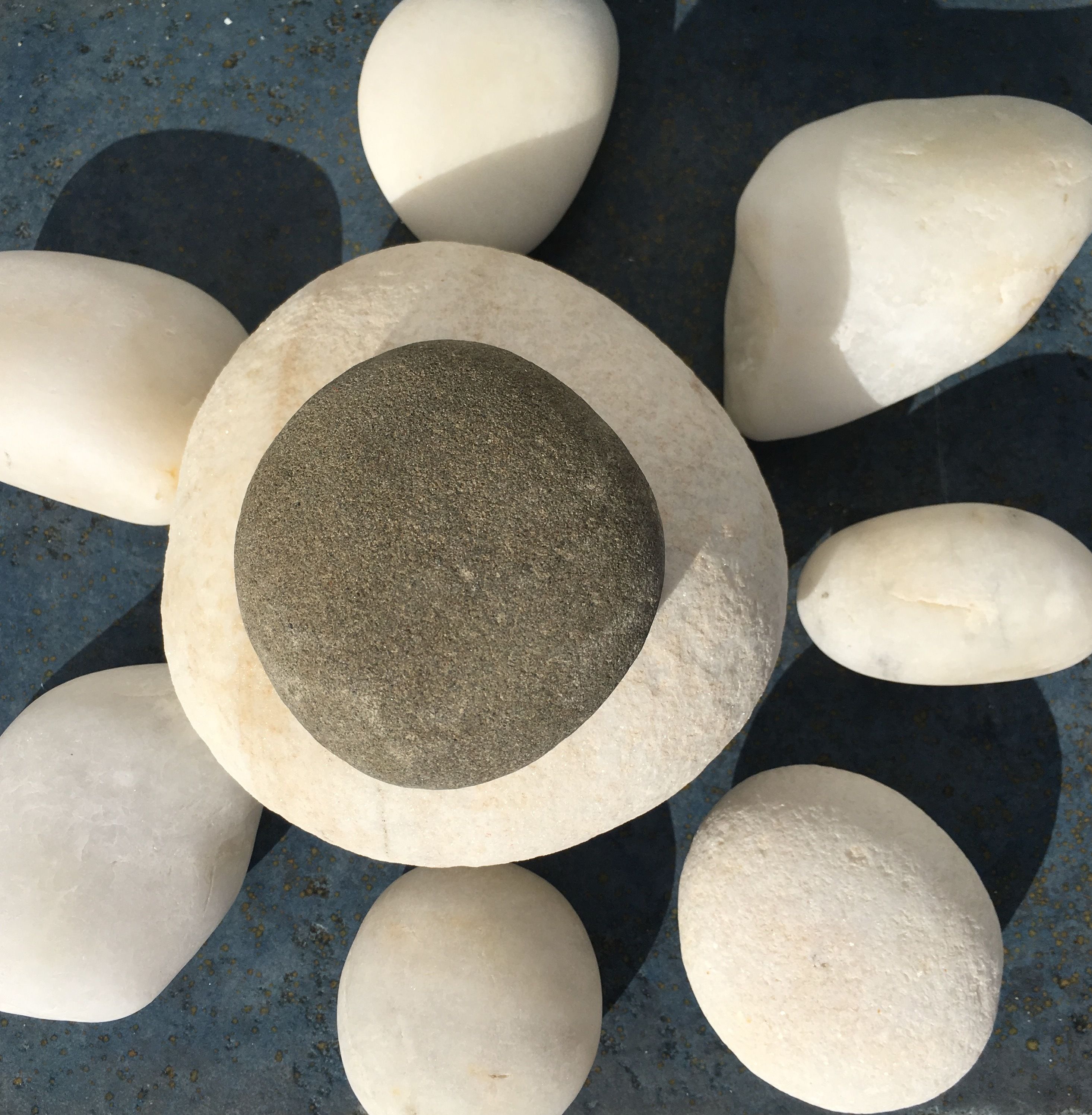Una estructura de piedra circular con una piedra central texturizada rodeada de piedras lisas sobre una superficie azul.