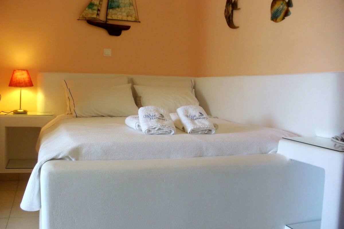 A neatly made bed with two folded towels, a lamp on a bedside table, and a wall-mounted sailboat decoration.