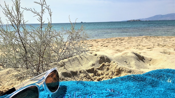 A beach with sand, a blue towel, and sunglasses. - Blue Harmony Apartments (Naxos)