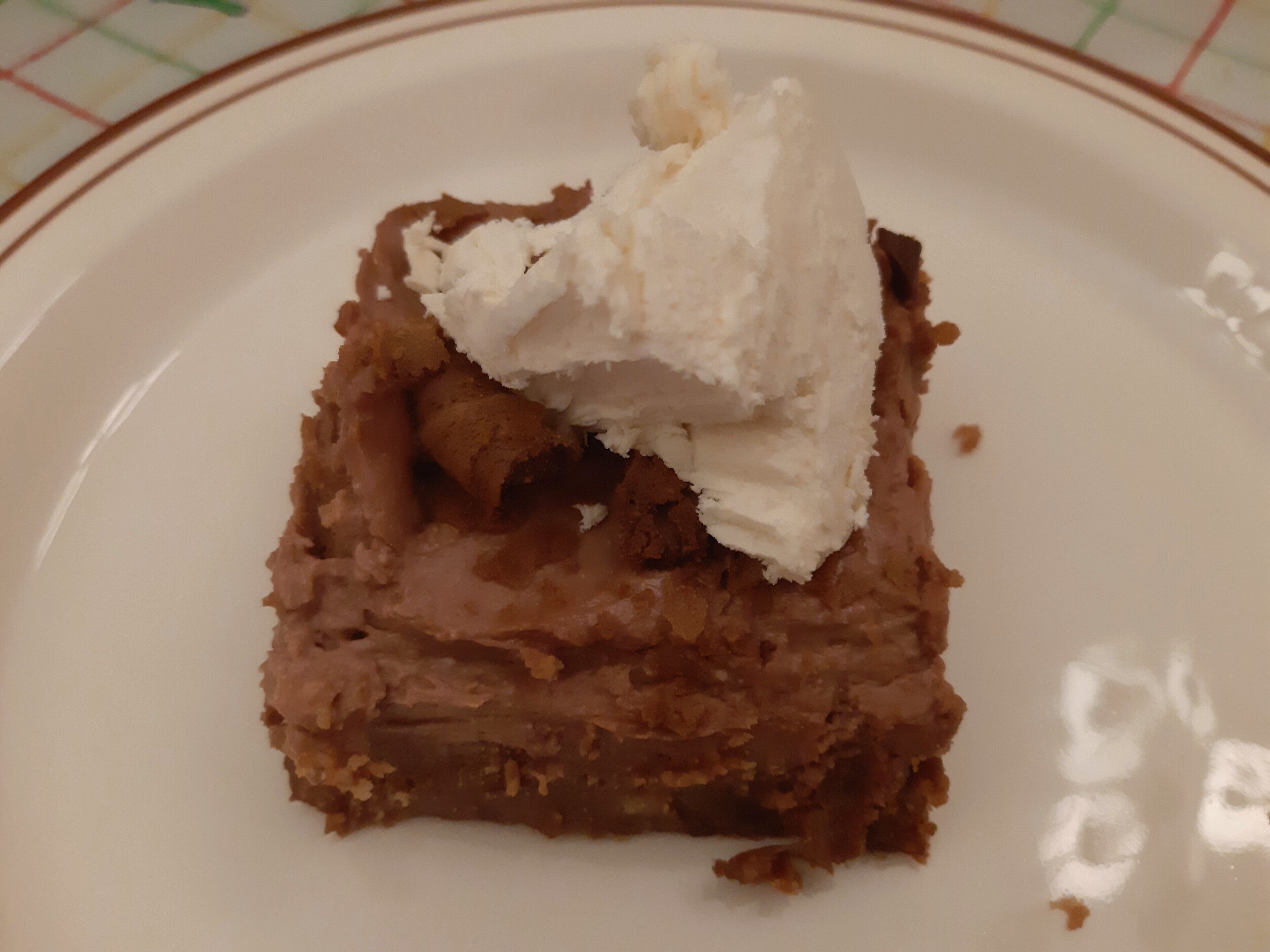 A piece of cake with a scoop of ice cream on top, placed on a white plate with a brown rim.