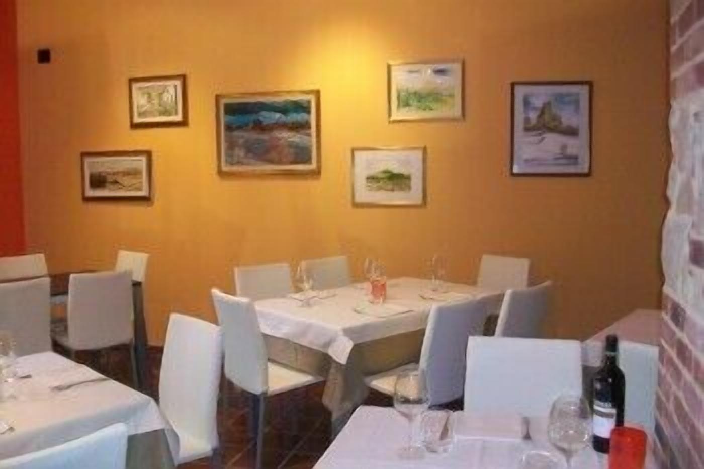 Ein Restaurant mit gedeckten Tischen, weißen Stühlen und gerahmten Kunstwerken an den Wänden.