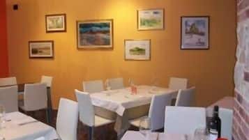Ein Restaurant mit gedeckten Tischen, weißen Stühlen und gerahmten Kunstwerken an den Wänden.