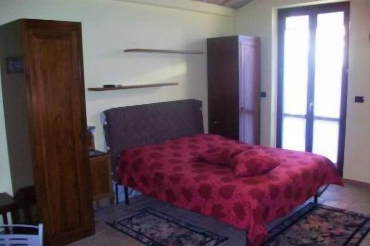 A bedroom with a bed, a wardrobe, a nightstand, and a window with curtains.