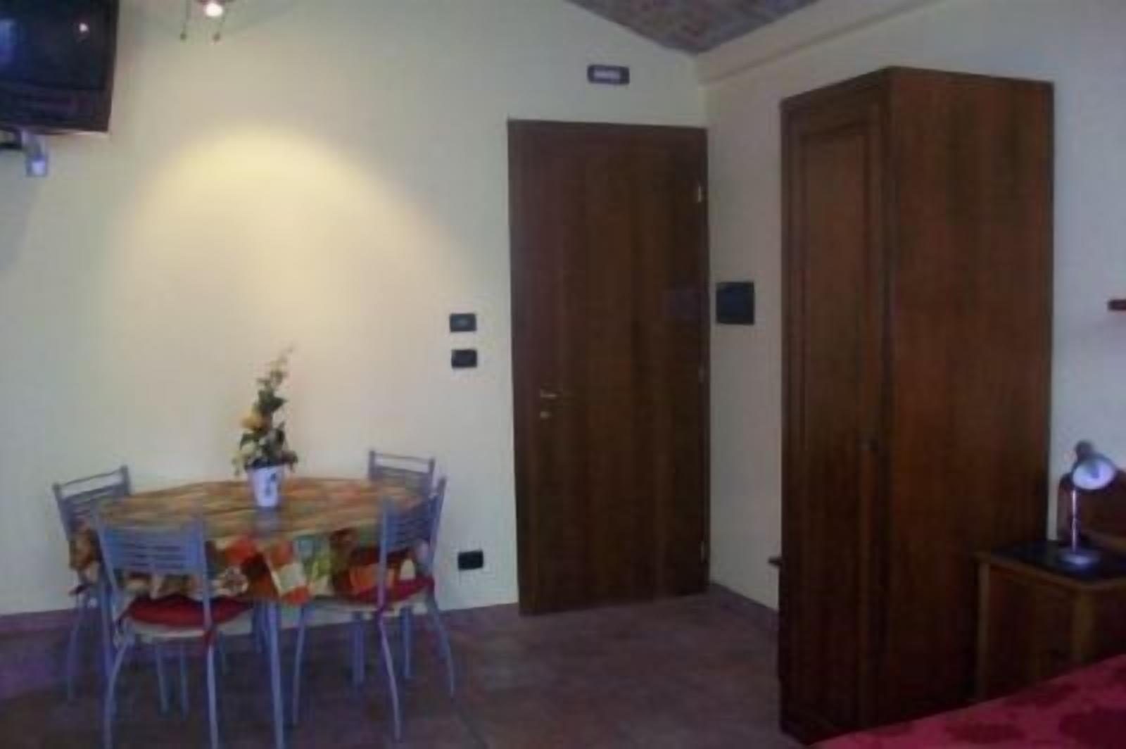 A dining area with a wooden table and chairs, a small plant, and a closed wooden door.