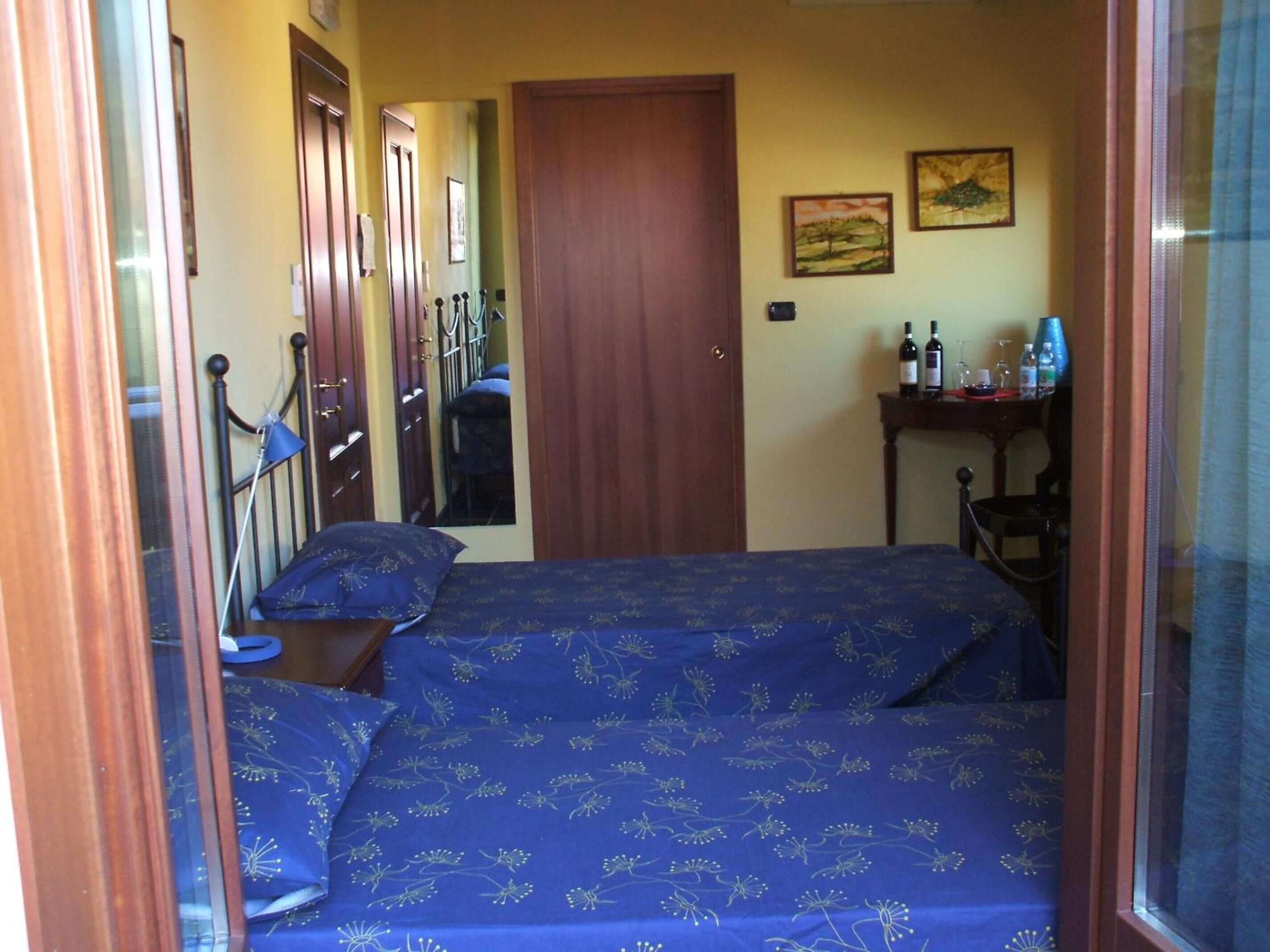 Una habitación pequeña y acogedora con una cama, un escritorio y una silla. Hay dos puertas y una ventana.