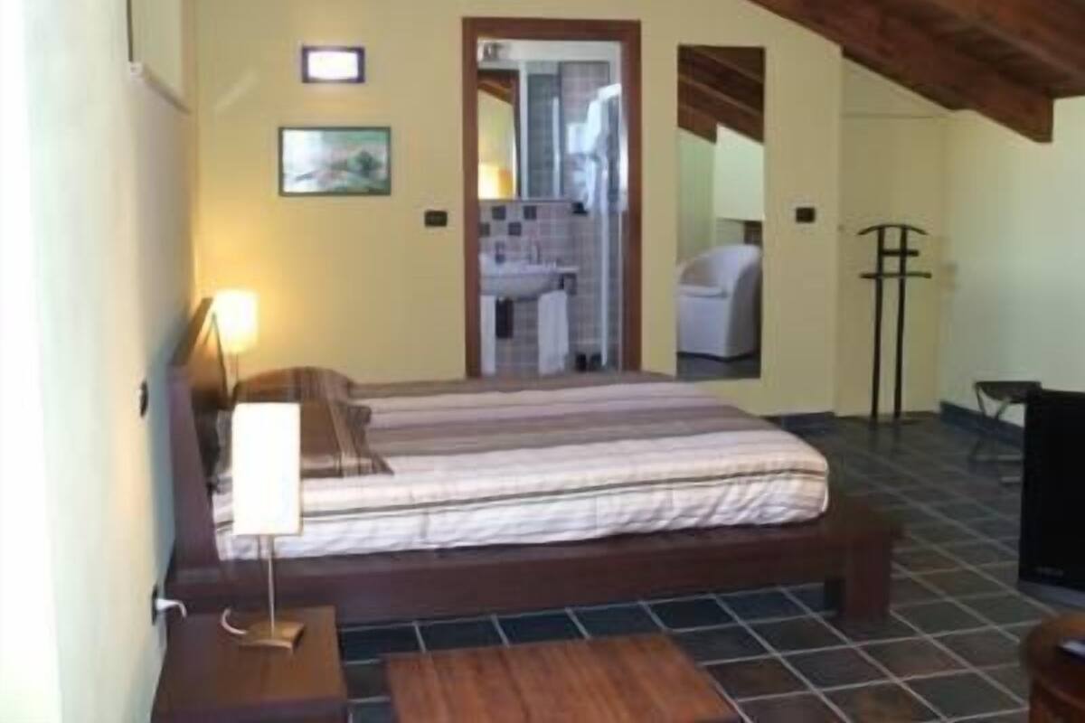 A bedroom with a bed, bedside table, lamp, and a view of a bathroom and a chair.