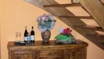 Eine Holztreppe mit Geländer, ein Holzschrank mit Weinflaschen und Gläsern sowie eine Vase mit Blumen.
