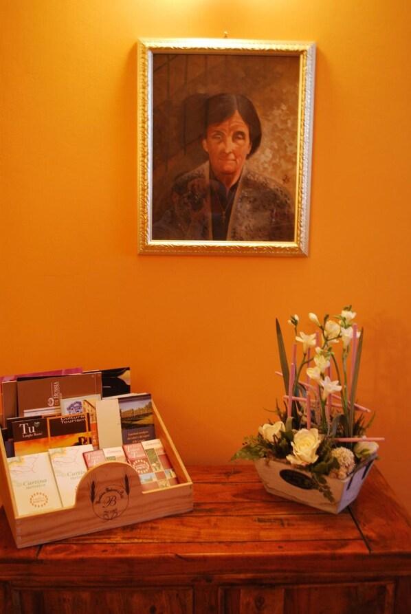 Une table en bois sur laquelle se trouvent un portrait encadré, une boîte de brochures de voyage et un vase de fleurs.