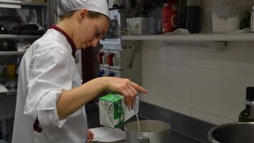 A chef in a white uniform pouring milk into a pot.