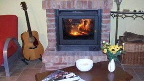 A living room with a fireplace, a guitar, a red chair, a table with a vase of flowers, and a basket.