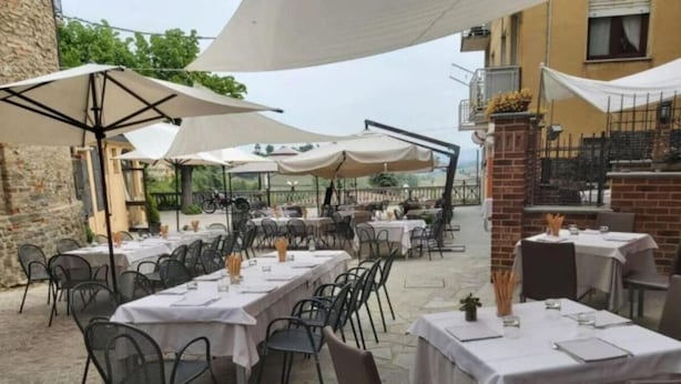 An outdoor dining area with tables and chairs, covered by umbrellas, set against a stone building.