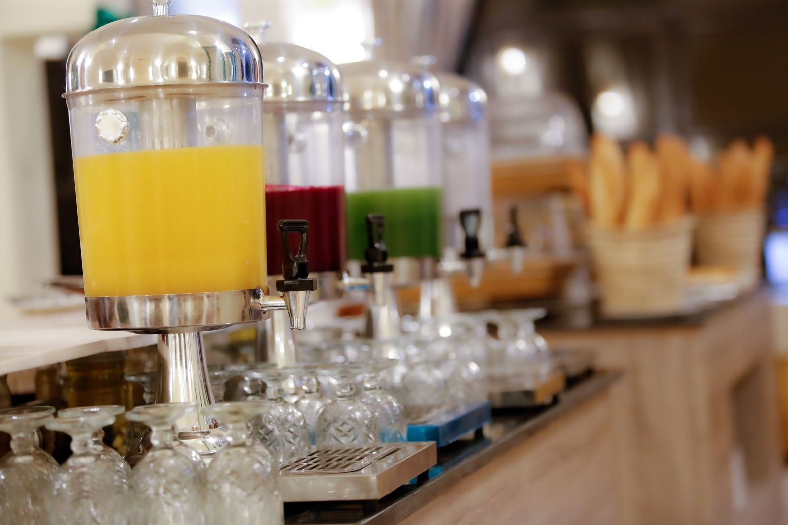 Un distributore automatico di bevande con diverse opzioni colorate, un vassoio di bicchieri e un cestino di pane.