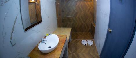A bathroom with a marble sink, wooden vanity, and a shower with a herringbone floor pattern.