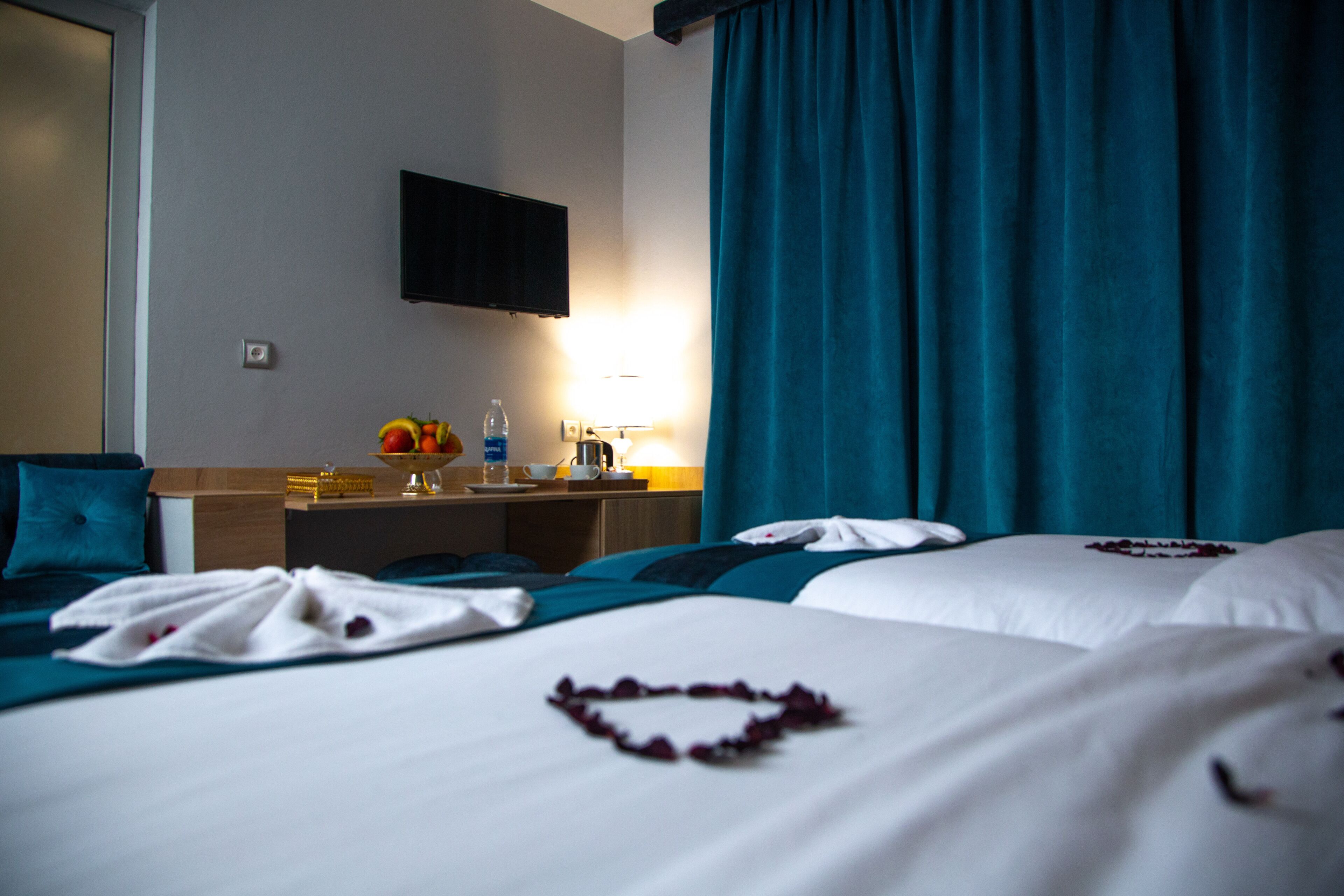 Une chambre d’hôtel avec deux lits, un téléviseur à écran plat fixé au mur, un bureau avec une lampe et une fenêtre avec des rideaux.