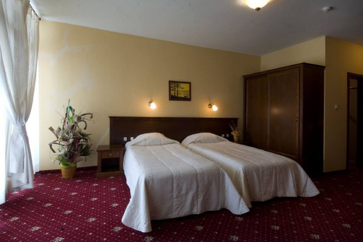 A hotel room with two beds, a wooden wardrobe, a small table, and a potted plant.
