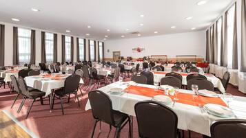 A large banquet hall with multiple round tables, each set with white tablecloths and orange runners.