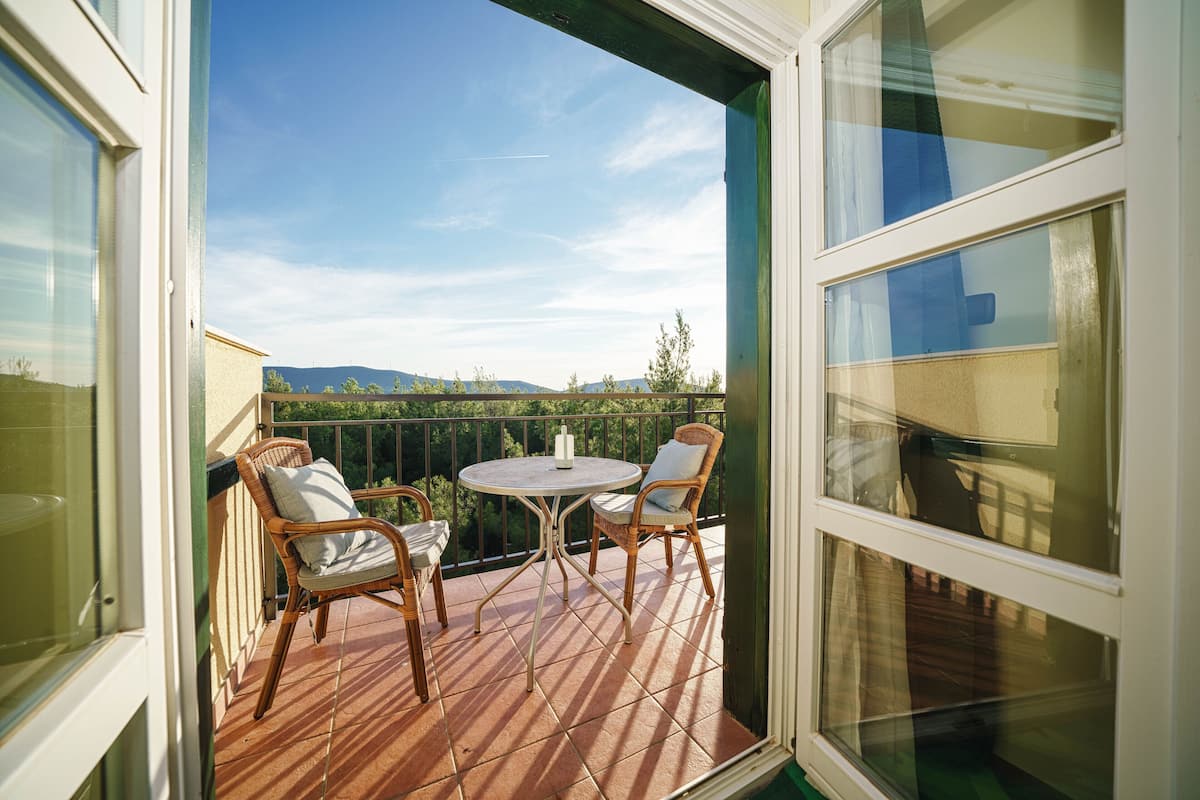 Ein offener Balkon mit Korbstühlen und einem kleinen Tisch, der einen Blick auf die umliegende Landschaft bietet.