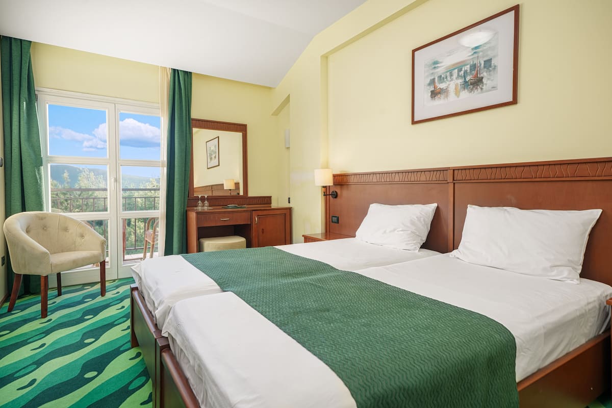 Ein Hotelzimmer mit zwei Betten, einem Sessel, einem Schreibtisch und einem Fenster mit Vorhängen.